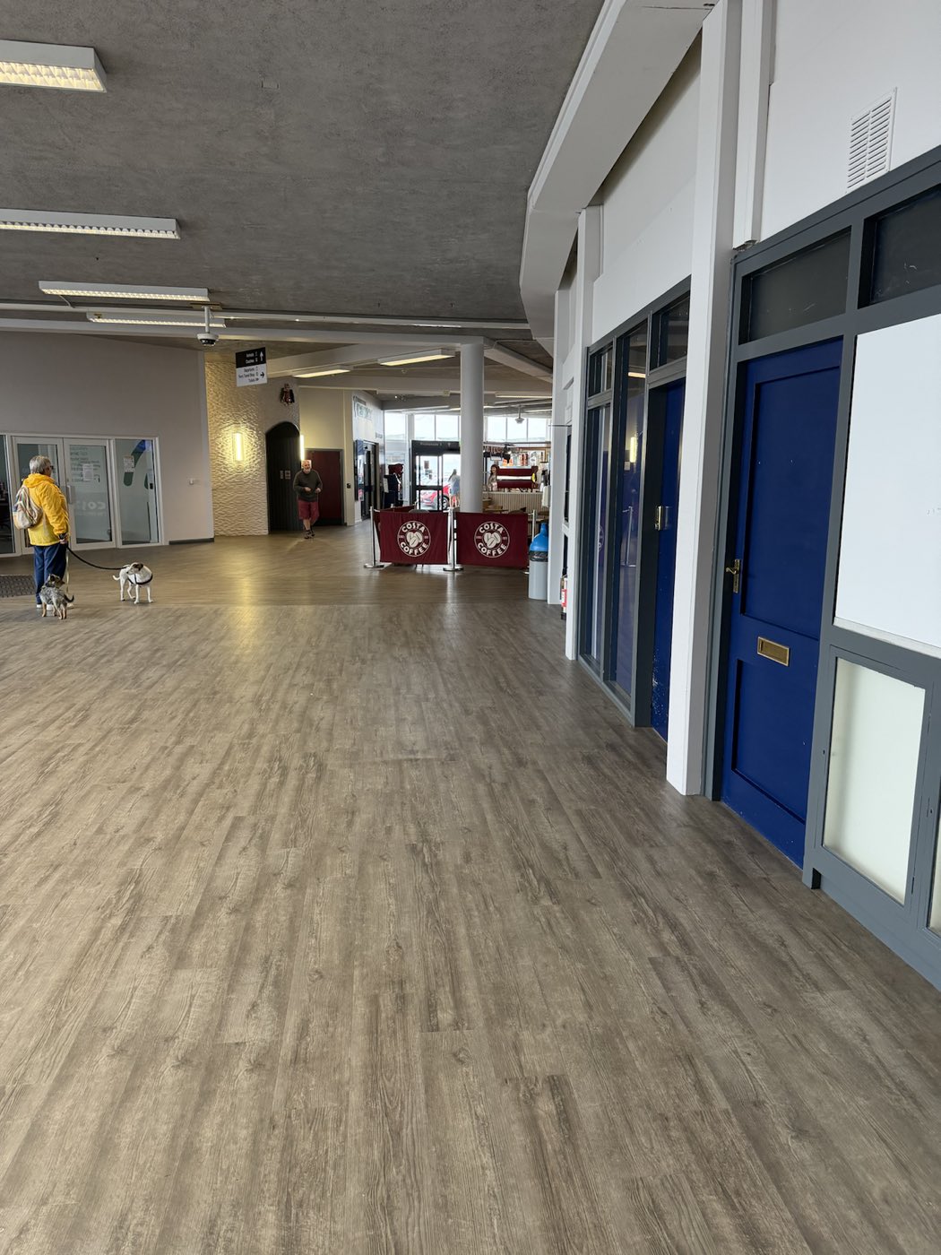 A wide commercial corridor with a freshly laid wood-plank luxury vinyl floor leading past navy-blue doors to an open seating area.