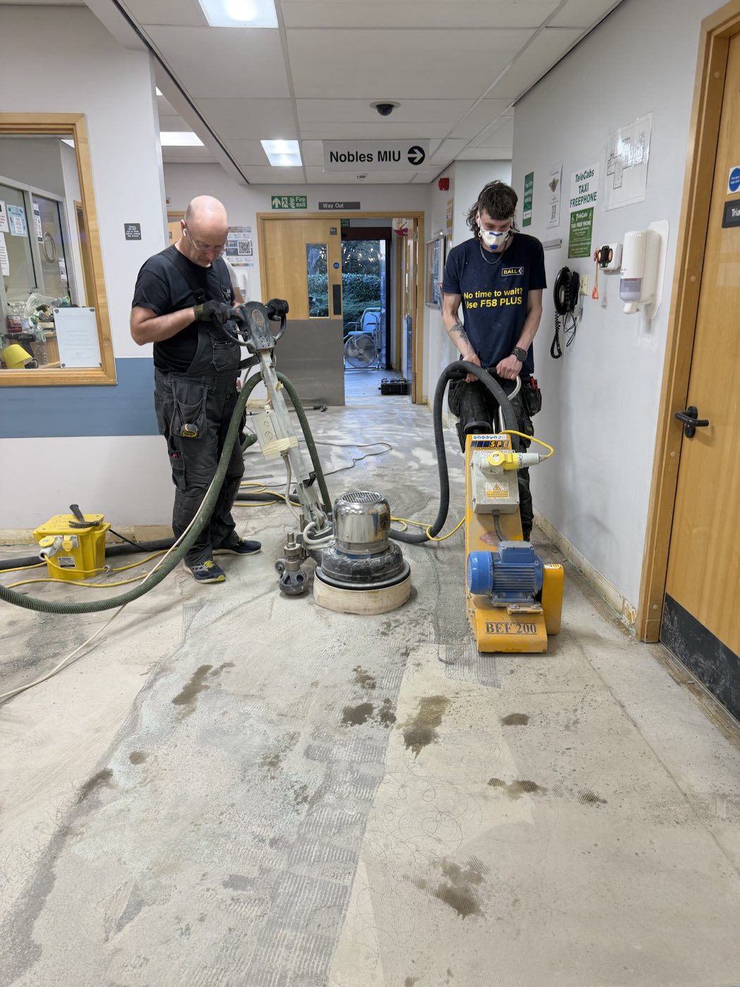 Two Swales fitters using floor grinding and preparation machines to take a healthcare corridor back to a clean, level subfloor ready for new flooring.