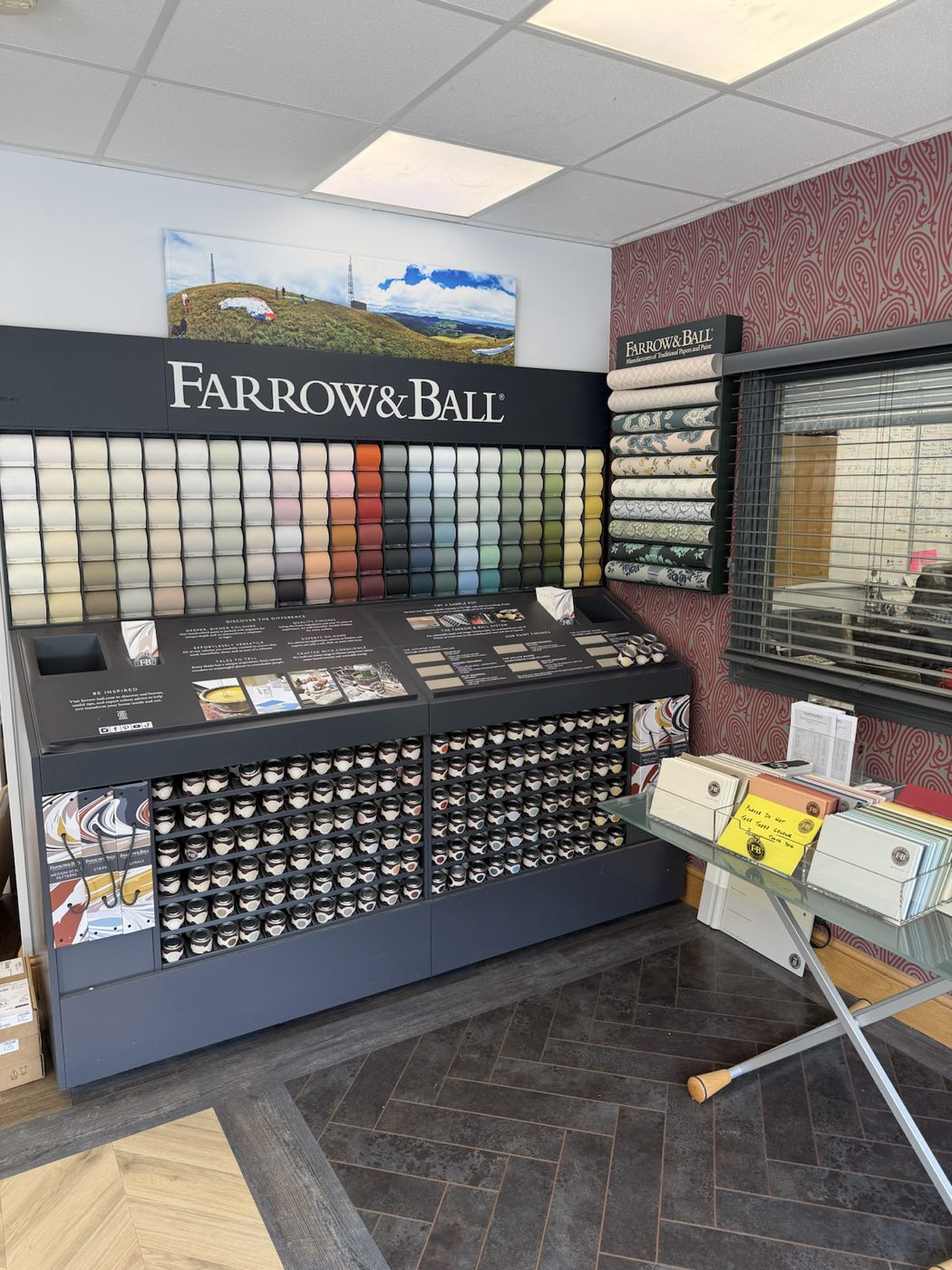 A corner of the Swales showroom in Laxey: the Farrow & Ball paint and wallpaper display set against a dark herringbone-laid floor.